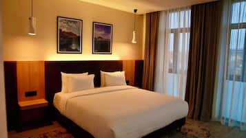 Una habitación de hotel con una cama grande, dos cuadros en la pared, una mesita de noche y una ventana con cortinas.