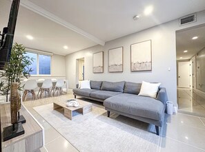 Ein modernes Wohnzimmer mit einem grauen Sofa, weißen Stühlen, einem Couchtisch und Kunstwerken an der Wand.