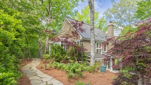Une maison avec un chemin de pierre menant à l’entrée, entourée d’une végétation luxuriante et d’arbres.
