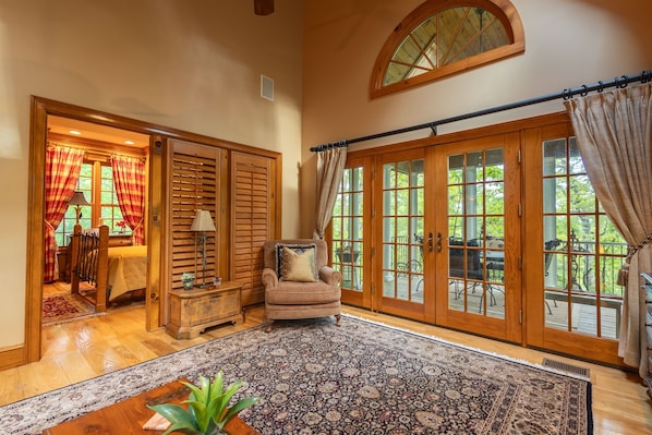 A spacious room with a large window, a cozy armchair, a wooden cabinet, and a patterned rug.