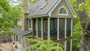 Une maison avec un porche couvert, un mur en pierre et un arbre.
