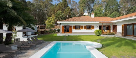A modern house with a swimming pool, surrounded by a well-maintained lawn and trees.