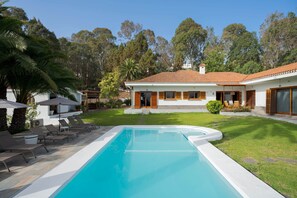 Una casa moderna con piscina, rodeada de un césped cuidado y árboles.