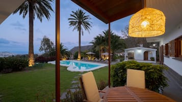 A covered outdoor area with a pool, lounge chairs, and a view of a mountain range.