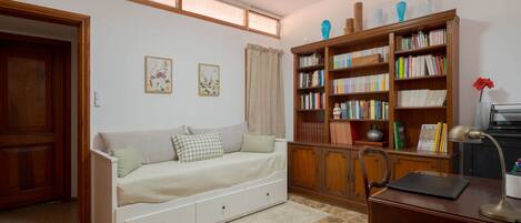 Una habitación con un sofá blanco, una estantería de madera, un escritorio con una lámpara y un suelo con diseño de piedra.