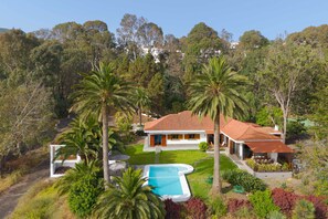 A house with a swimming pool, surrounded by palm trees and a garden.