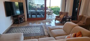 A living room with a TV, sofa, armchair, and a view of a patio with a table and chairs. - Exclusive Villa Mirador de Arucas - Family & Friends (Arucas)