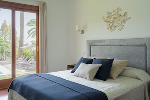 A bedroom with a bed, a nightstand, a wall-mounted lamp, and a view of an outdoor pool area.