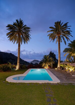 A swimming pool with lounge chairs and palm trees, surrounded by a landscaped garden.
