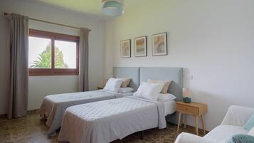 A room with two beds, a nightstand, a window with curtains, and framed pictures on the wall.