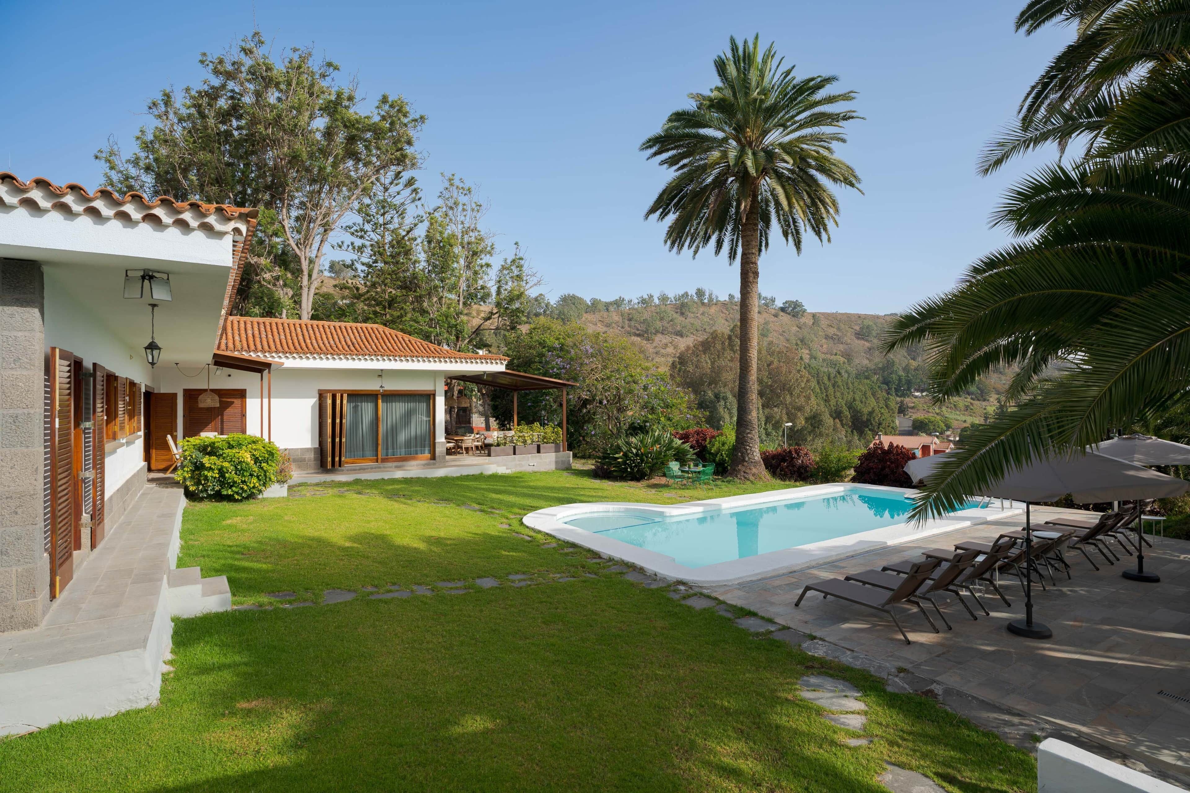 Ein Haus mit Schwimmbad, einer Terrasse mit Liegestühlen und Blick auf die Hügel.