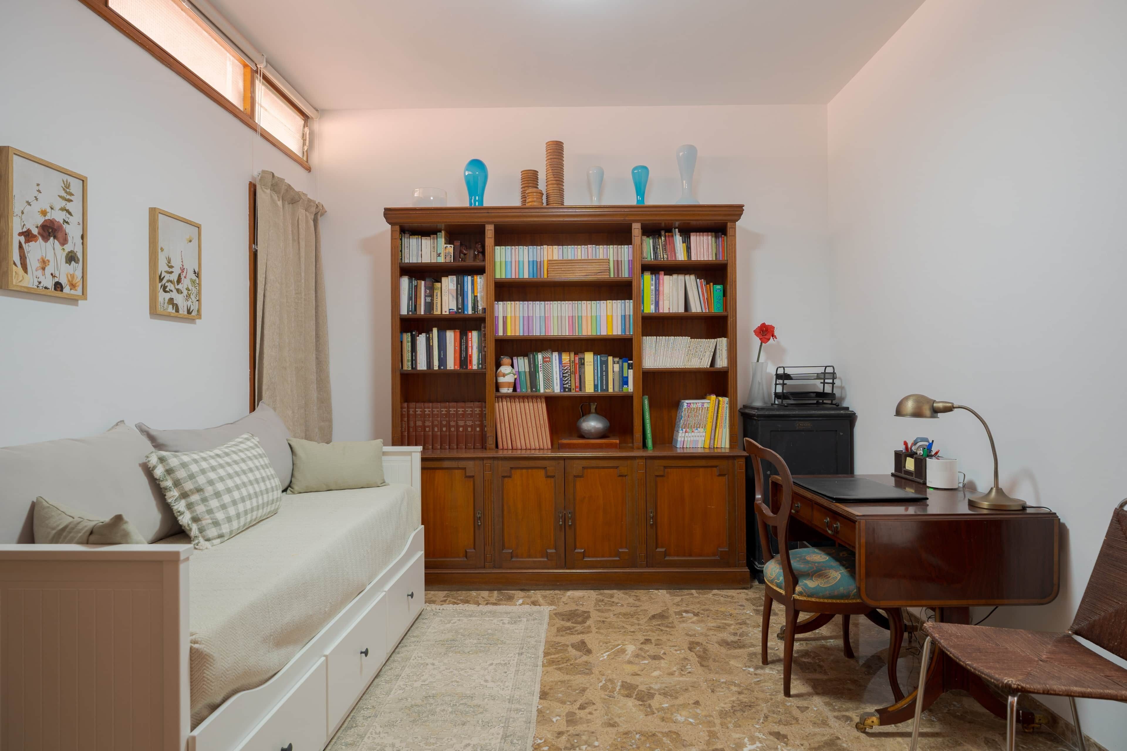 A cozy room with a wooden bookshelf, a desk, a chair, a sofa, and a small table with a lamp.