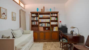 A cozy room with a wooden bookshelf, a desk, a chair, a sofa, and a small table with a lamp.