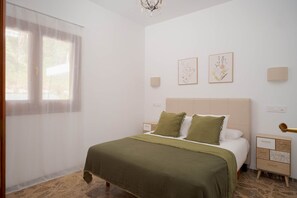A bedroom with a bed, bedside tables, a nightstand, a chandelier, and artwork on the wall.