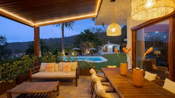 Un espace extérieur aménagé avec des sièges, une piscine, du mobilier en bois et une vue sur une colline.