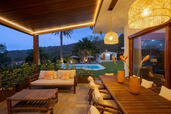 An outdoor seating area with a pool, wooden furniture, and a view of a hill.