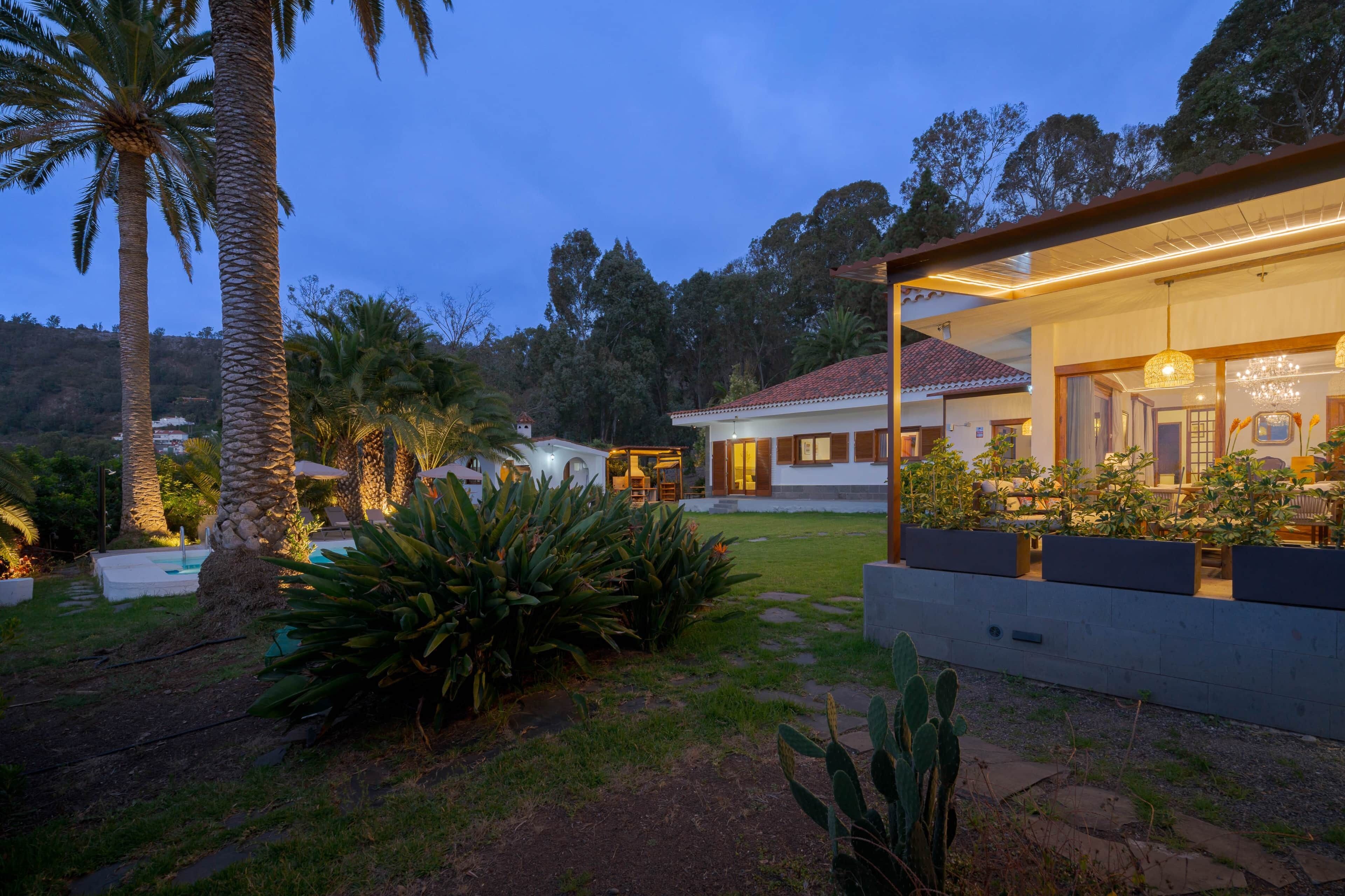 Una casa moderna con piscina, circondata da piante tropicali e un cielo sereno.