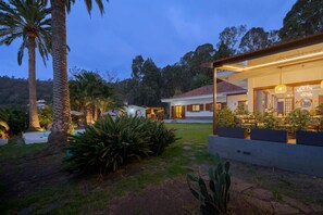 Una casa moderna con piscina, rodeada de plantas tropicales y un cielo despejado.
