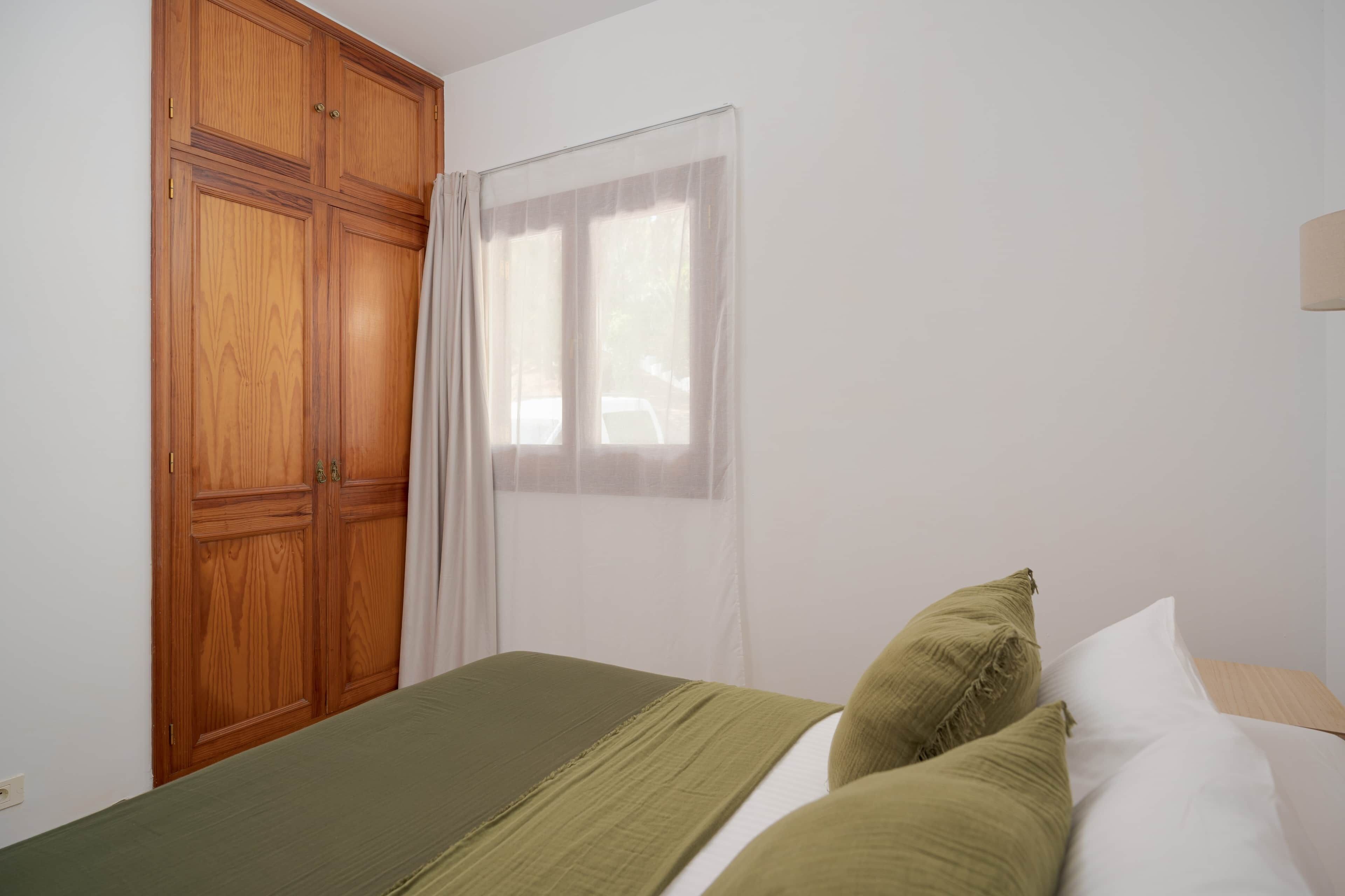 Une chambre à coucher avec un lit, une armoire en bois et une fenêtre avec des rideaux.