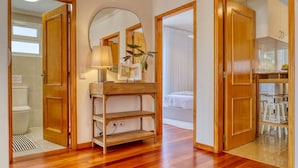 A room with wooden flooring, a mirror, a wooden shelf, a bed, and a table with stools. - Funchal Infinity, a Home in Madeira (Funchal)