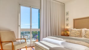 A bedroom with a bed, a chair, a nightstand, and a view through a glass door. - Funchal Infinity, a Home in Madeira (Funchal)