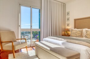 A bedroom with a bed, a chair, a nightstand, and a view through a glass door. - Funchal Infinity, a Home in Madeira (Funchal)