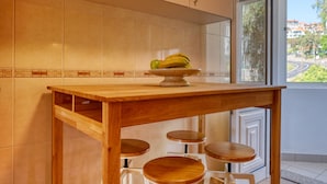 A kitchen with a wooden table, three stools, and a fruit bowl on the counter. - Funchal Infinity, a Home in Madeira (Funchal)
