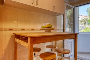 A kitchen with a wooden table, three stools, and a fruit bowl on the counter. - Funchal Infinity, a Home in Madeira (Funchal)