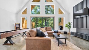 A spacious living area with a high ceiling, large windows, a pool table, and a fireplace. - A-Frame Retreat with Pool, Hot Tub, Lake Access (Garland County)
