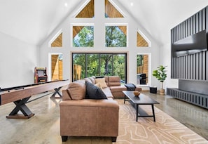 A spacious living area with a high ceiling, large windows, a pool table, and a fireplace. - A-Frame Retreat with Pool, Hot Tub, Lake Access (Garland County)