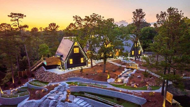 A modern house with a unique architectural design, surrounded by a landscaped garden with pathways and a small waterfall feature. - A-Frame Retreat with Pool, Hot Tub, Lake Access (Garland County)