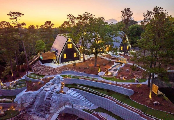 A modern house with a unique architectural design, surrounded by a landscaped garden with pathways and a small waterfall feature. - A-Frame Retreat with Pool, Hot Tub, Lake Access (Garland County)