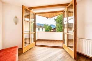 Una habitación con piso de madera, un banco rojo y vistas a una montaña y árboles a través de amplios ventanales.