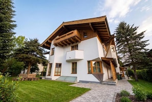 Une maison à deux étages avec un balcon en bois, une allée pavée et une pelouse bien entretenue.
