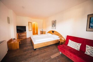 A hotel room with a bed, a red sofa, a TV, a bedside table, and a wall-mounted lamp. - Vrbo Property (Zell am See)