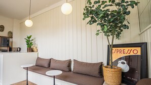 Un interior moderno con un sofá, dos mesas auxiliares, una planta colgante y un letrero enmarcado que dice 'espresso'.