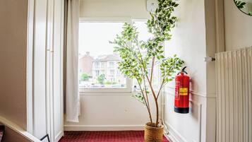 Un pasillo con un extintor rojo, una planta en maceta y un radiador.