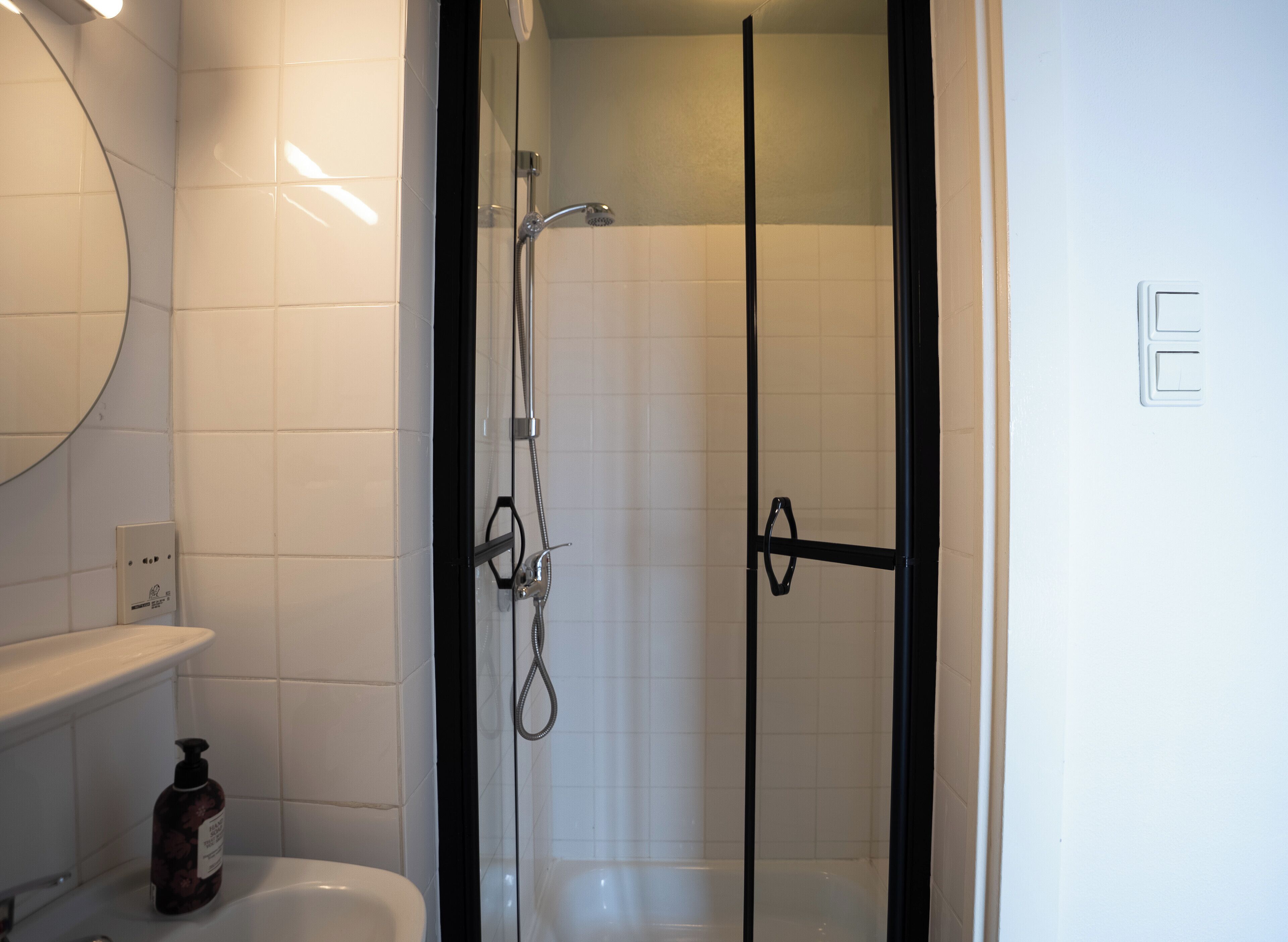 Ein Badezimmer mit einer gläsernen Duschkabine, einer weißen Toilette und einem Spiegel über dem Waschbecken.