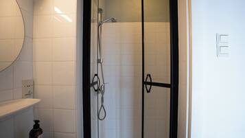 Ein Badezimmer mit einer gläsernen Duschkabine, einer weißen Toilette und einem Spiegel über dem Waschbecken.