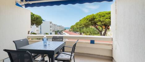 A balcony with a table and chairs, a view of the sea, and buildings in the background.