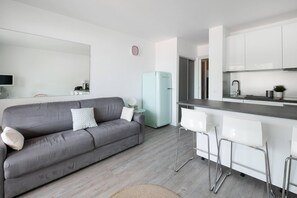 Un salon moderne avec un canapé gris, un réfrigérateur bleu clair et un coin cuisine doté de tabourets de bar blancs.