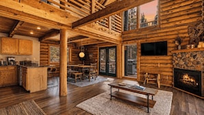 L’intérieur d’une cabane en rondins comprend un coin repas, une cuisine, une cheminée et de grandes fenêtres.