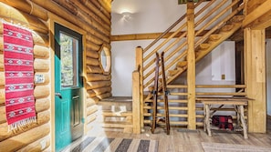 A log cabin interior with a wooden staircase, a green door, and a patterned rug.