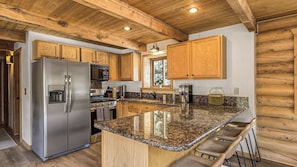 A modern kitchen with wooden cabinets, stainless steel appliances, granite countertops, and a bar area.