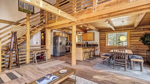 A log cabin interior with a kitchen, dining area, and a staircase.