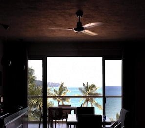 A room with a ceiling fan, large windows, and a view of the ocean.