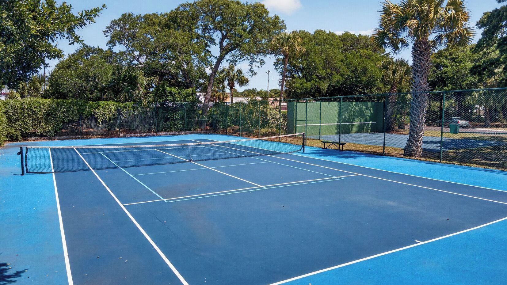 A tennis court with a net, surrounded by trees and a fence.