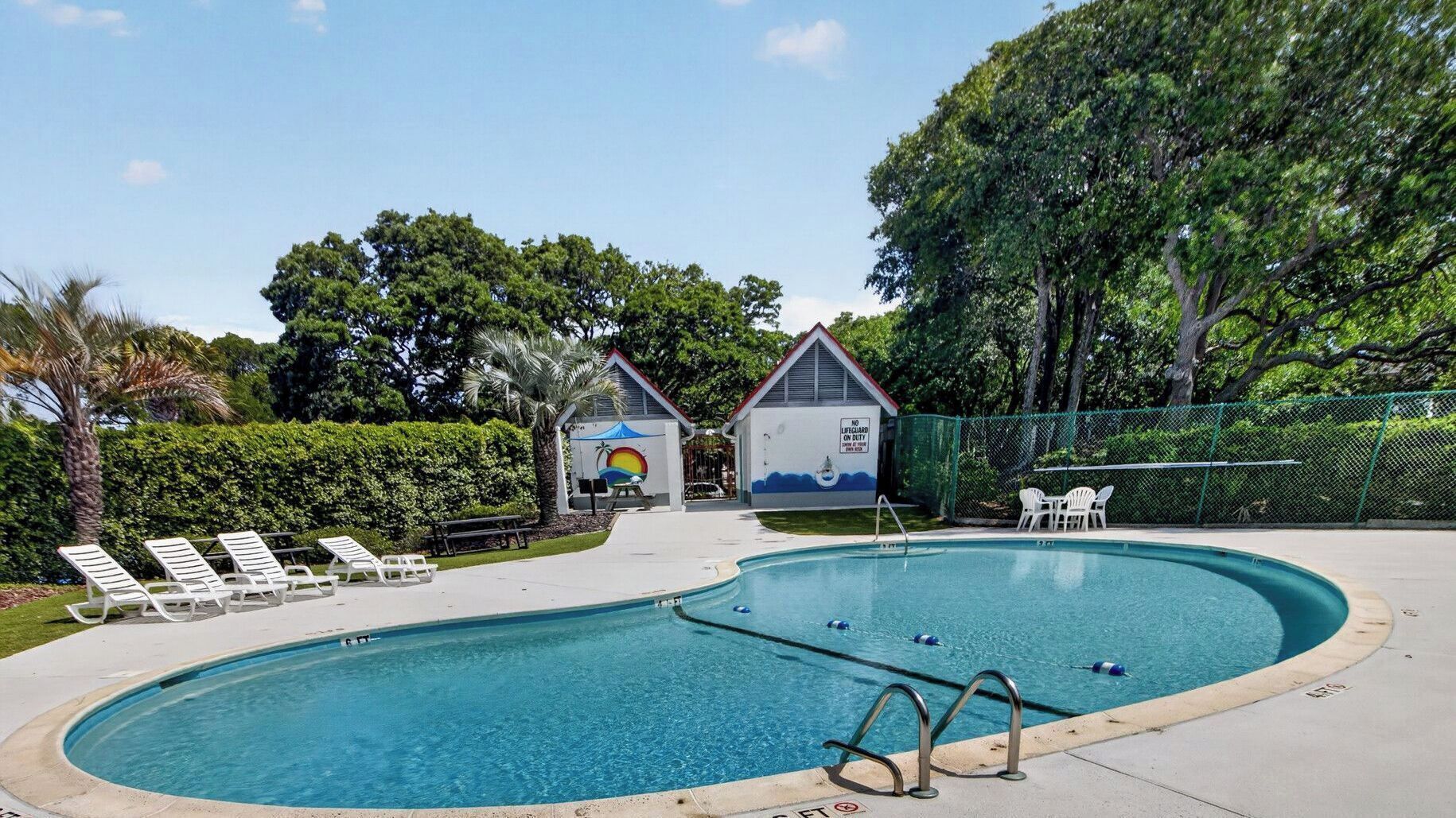 Ein Schwimmbecken mit Liegestühlen, einem Rettungsschwimmerstand und einem kleinen Gebäude mit Wandgemälde.