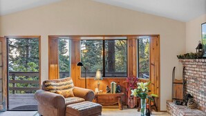 Una habitación acogedora con chimenea, muebles de madera y ventanas amplias que dan a árboles.