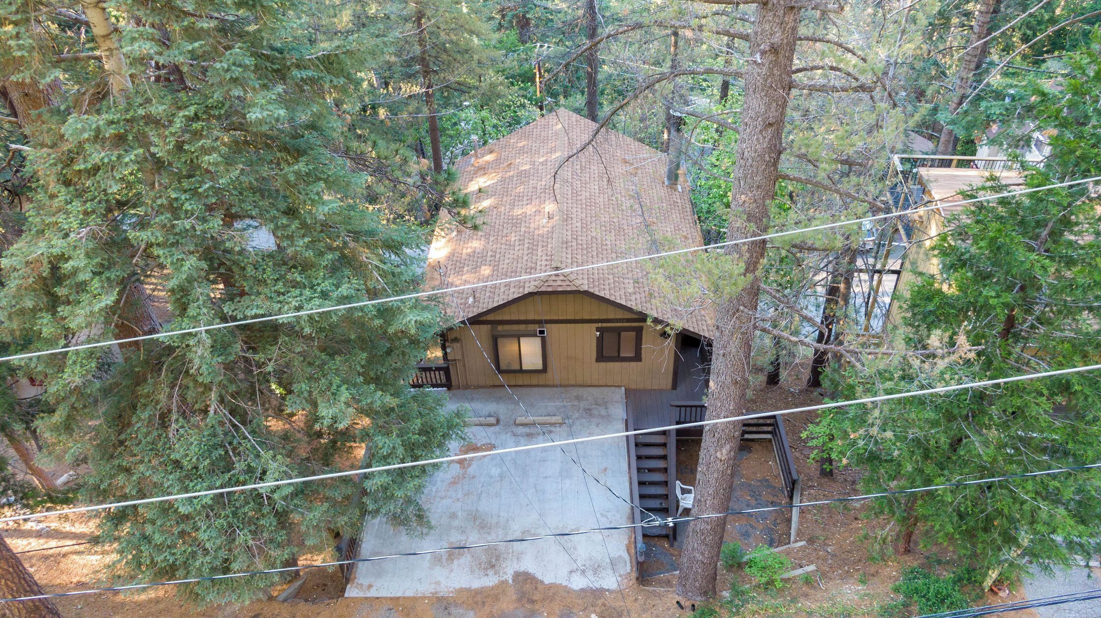 Une petite cabane en bois d’un seul étage, entourée d’arbres, avec des fondations en béton et un toit en pente.
